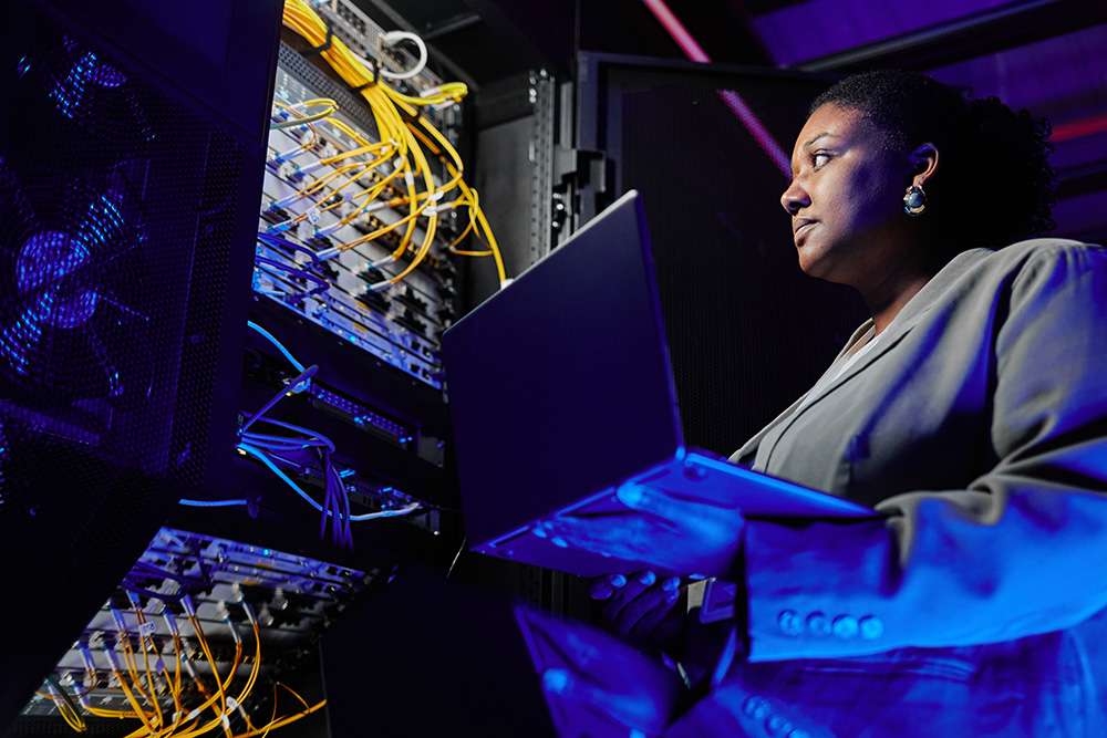 CompTIA Server+ candidate with laptop in data center. IT professional managing servers.