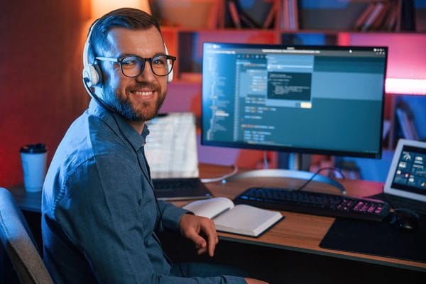 Front-End Engineer at desk with code on screen. Developer with headphones smiling. Software development job.