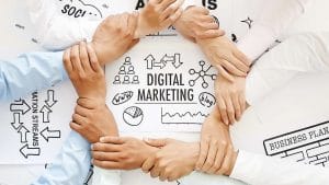 Teamwork in digital marketing. Hands linked around Digital Marketing sketches, social media, analysis, & business plan.
