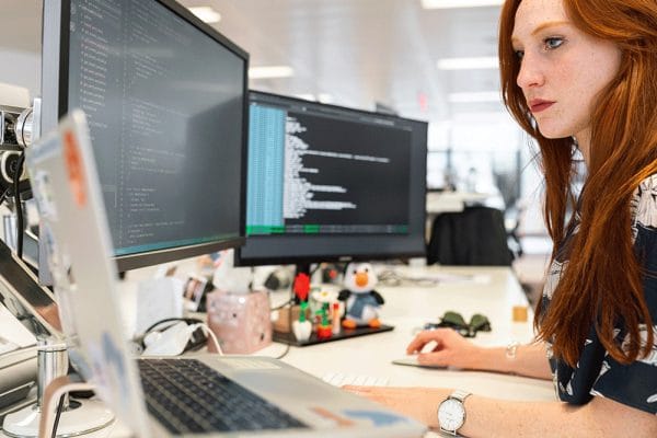 Microsoft Azure infrastructure design. Woman works on Azure solutions with dual monitors displaying code.