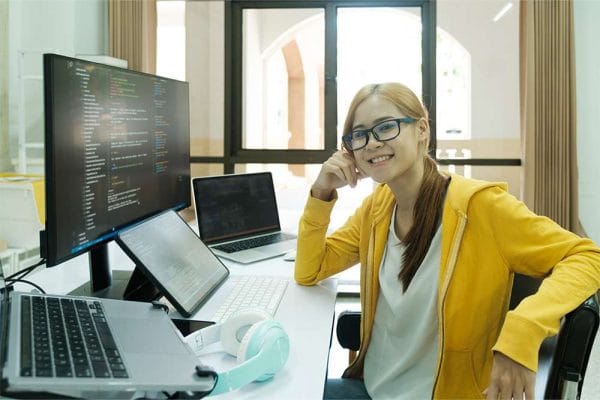 Microsoft Azure Administrator (AZ-104) candidate smiling at desk with multiple computers and coding on screen.