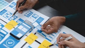 Android mobile development: App designers planning UI/UX with layouts and sticky notes.
