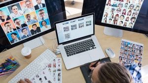 Web design: Designer working with a graphic tablet, laptop, and dual monitors displaying diverse faces.