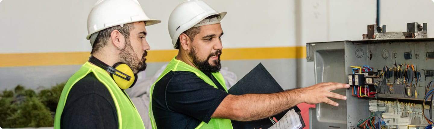 Learnerships: Workers in safety gear inspect electrical panel. Training and development in action.