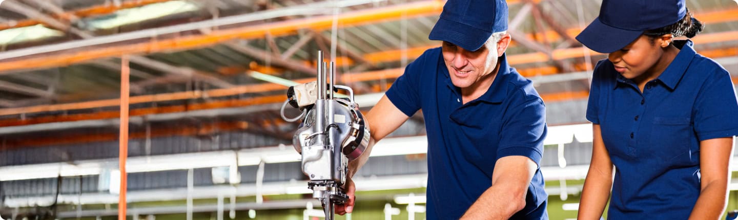Two workers in blue uniforms using machinery. Skills development support.