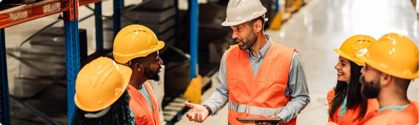 Workforce training. Workers in safety vests and hard hats receiving on-the-job training in a warehouse.
